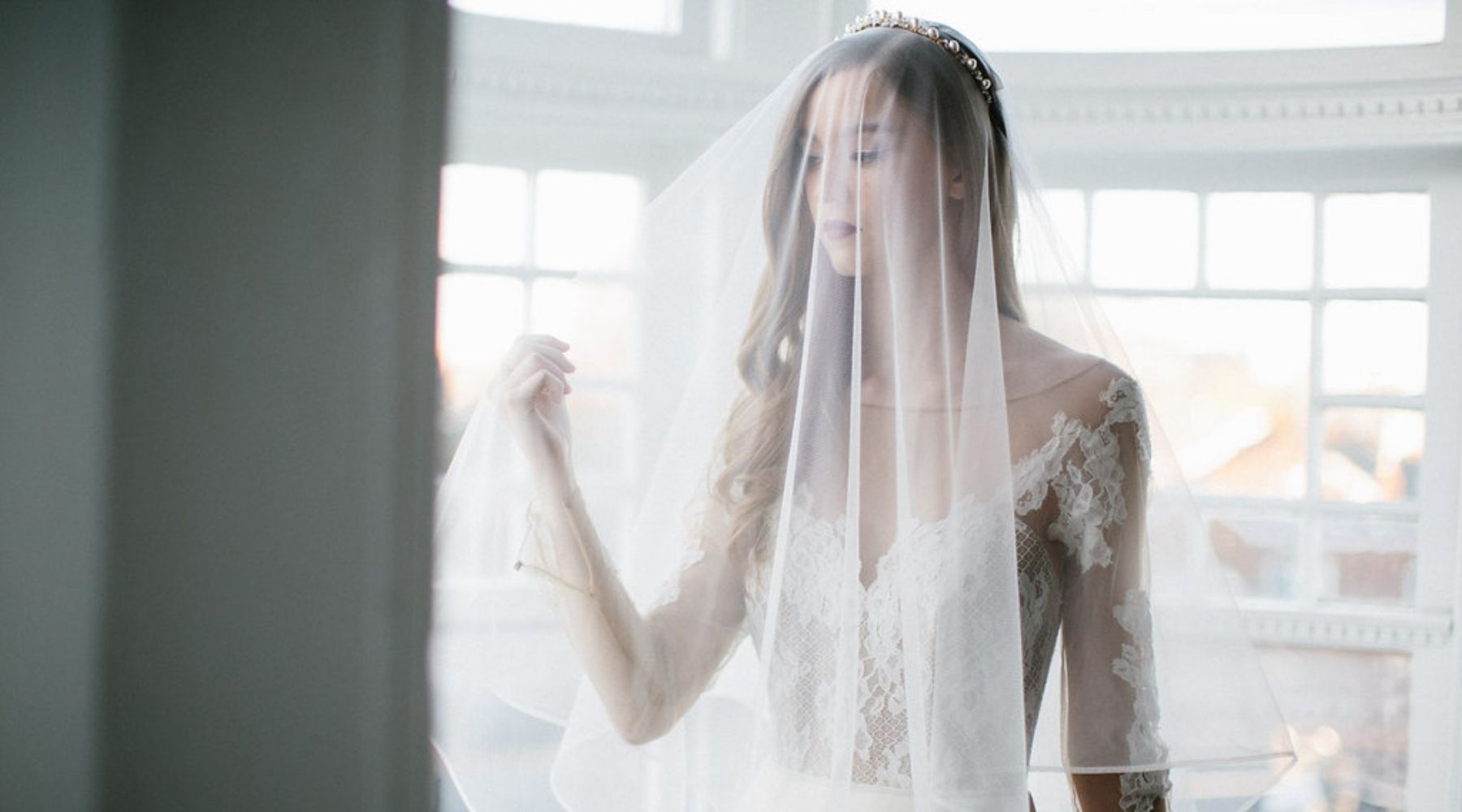 bride standing by the window in a veil covering face