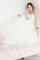 Bride seated wearing hand embroidered floral Indra Cathedral Veil with train cascading over the side of the sofa.