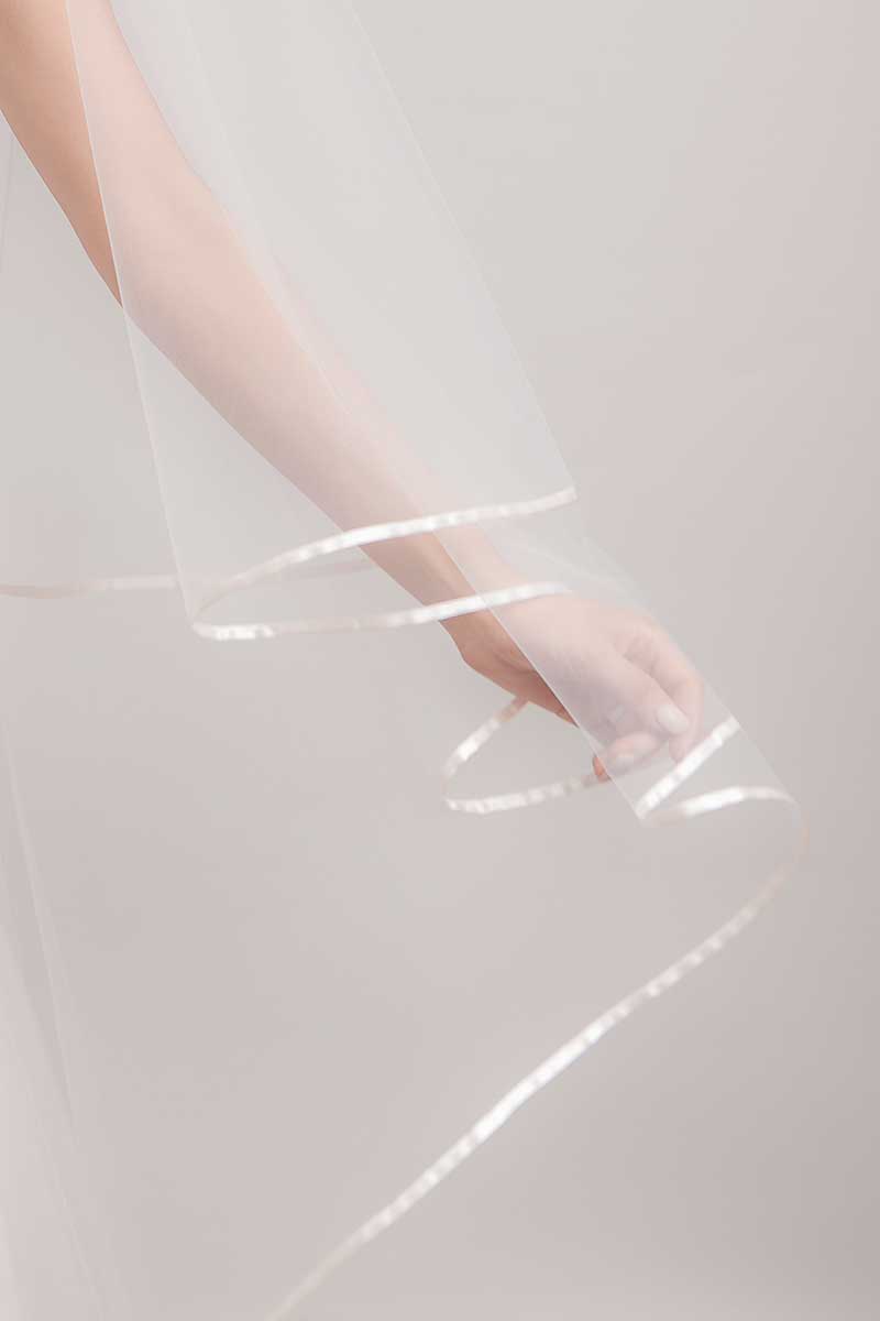 Arm of bride holding out satin ribbon edge of cathedral length veil by Laura Jayne. Miranda Ribbon Edge Cathedral Veil. Handmade in Canada.