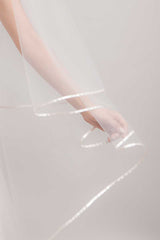 Arm of bride holding out satin ribbon edge of cathedral length veil by Laura Jayne. Miranda Ribbon Edge Cathedral Veil. Handmade in Canada.