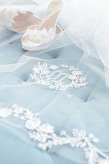 Close up of embroidered monogram cathedral wedding veil details with bridal shoes in background. Khrysia Monogram Cathedral Veil by Laura Jayne. Handcrafted in Toronto, Canada.