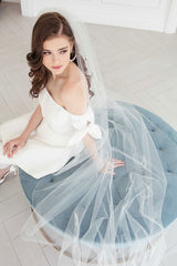 Stylish modern bride seated wearing whimsical feather and crystal cathedral length wedding veil. Winona Cathedral Veil with Feathers. Laura Jayne Accessories Toronto. Handcrafted in Canada.