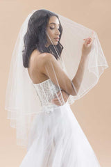 Bride wearing strapless wedding gown and sheer blusher veil with pearl and crystal details along the border. Jess Beaded Edge Fingertip Veil by Laura Jayne Accessories. Handcrafted in Toronto, Canada.