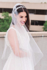 Bride wearing a sheer fingertip length wedding veil with mixed pearls. Pandora Pearl Fingertip Veil by Laura Jayne. Handcrafted in Canada.