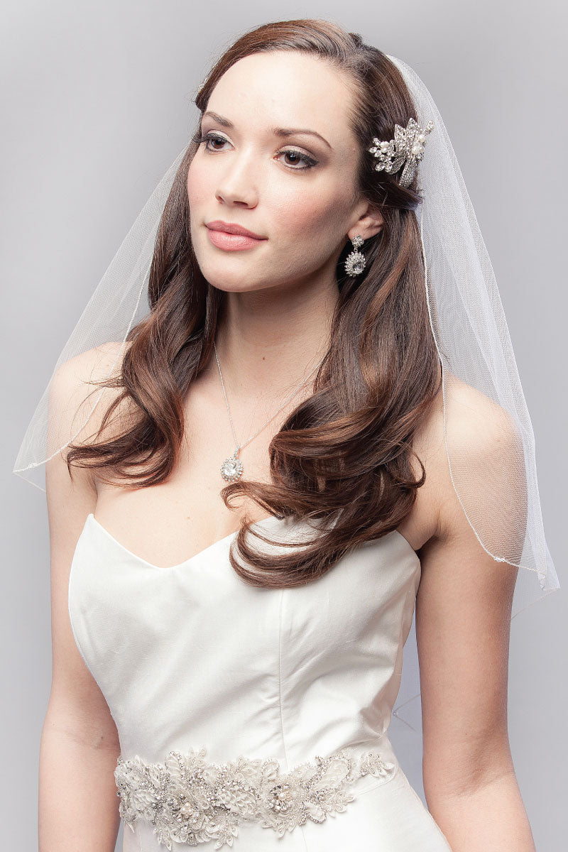 Pretty bride wearing cascade cut fingertip length tulle veil with crystal accents and silver metallic edging. Embrace Cascade Fingertip Veil. Laura Jayne Accessories Toronto. Handcrafted in Canada.