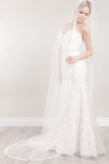 Full length view of a beautiful modern bride wearing a timeless classic long veil with French Alencon lace scalloped border, hand-beaded crystals and romantic floating appliques on the train. Promise Lace Cathedral Veil. Made in Toronto, Canada by Laura Jayne Accessories..