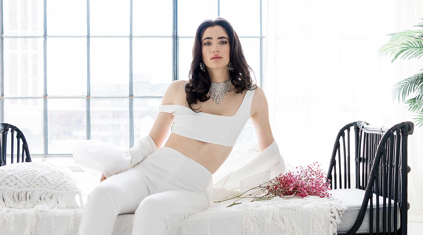 Woman lounging on bed in urban loft wearing white bridal separates & Laura Jayne Accessories