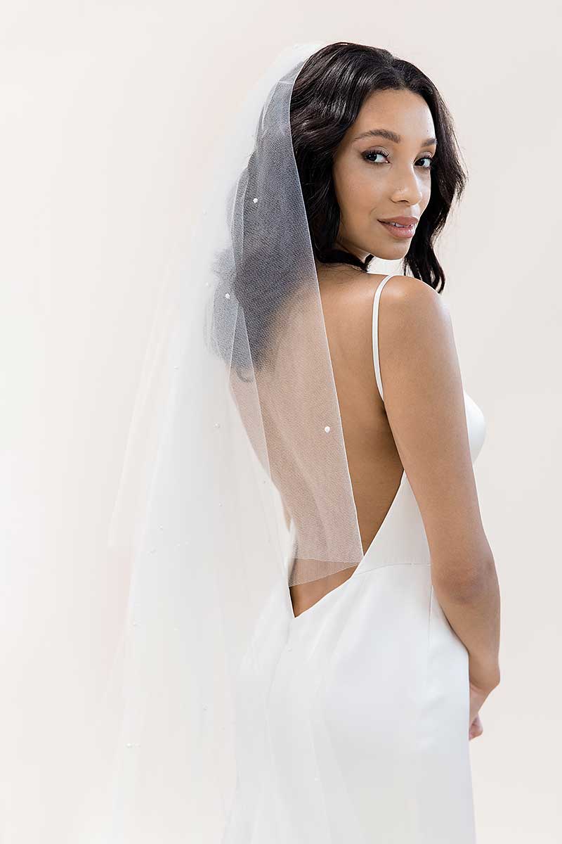 Bride looking over shoulder wearing Alayna pearl beaded oval cut cathedral drop veil by Laura Jayne Accessories. Made in Toronto, Canada.