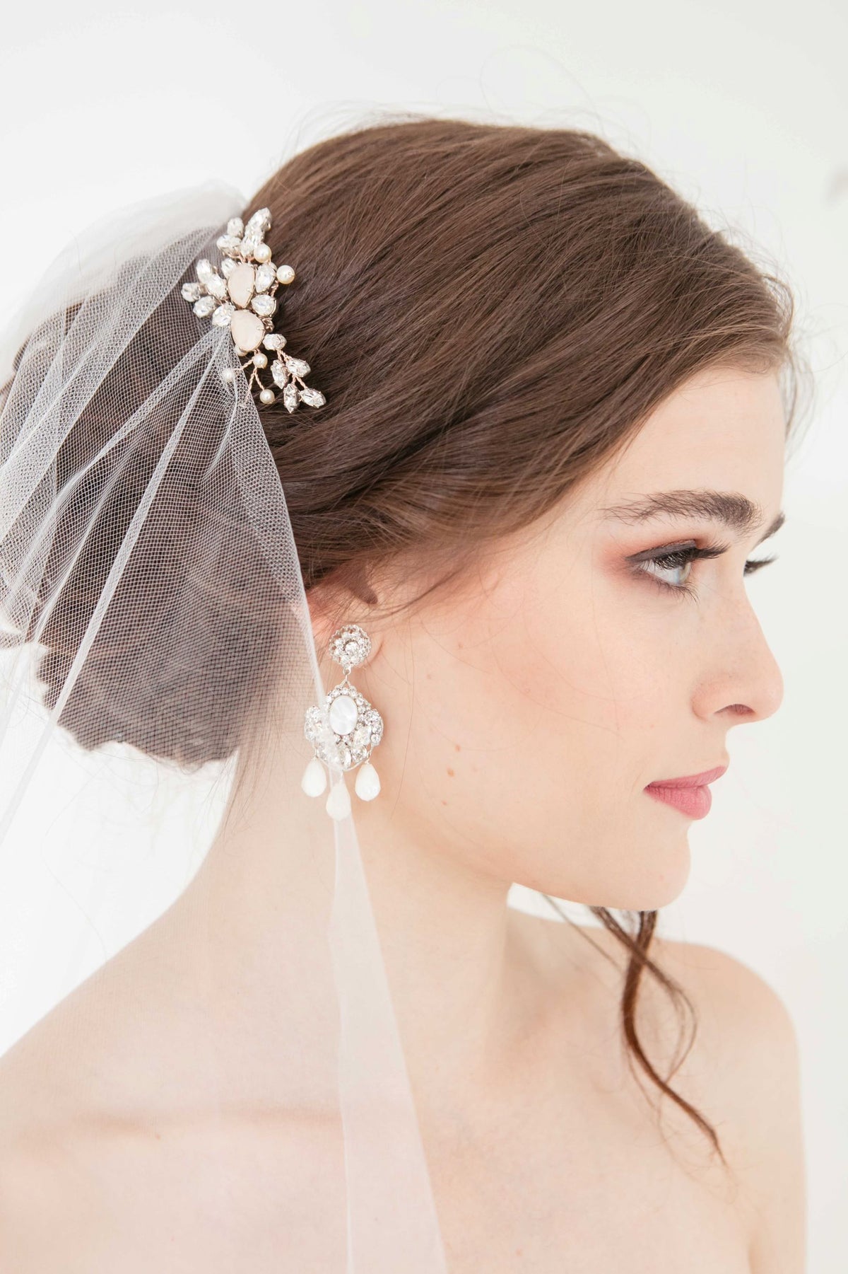 Rose gold crystal profile wedding hair comb on woman with statement drop earrings and veil