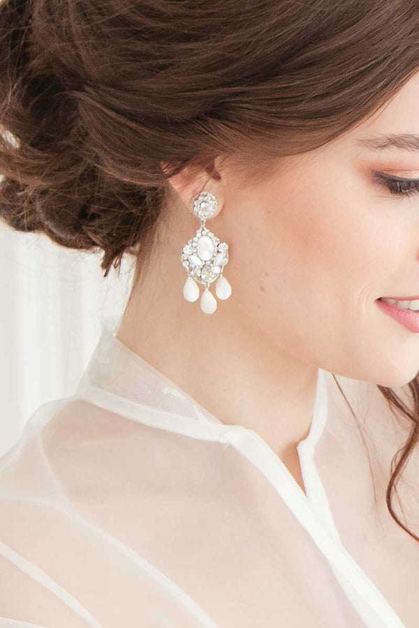 Woman wearing statement crystal earrings with faceted mother of pearl drops.