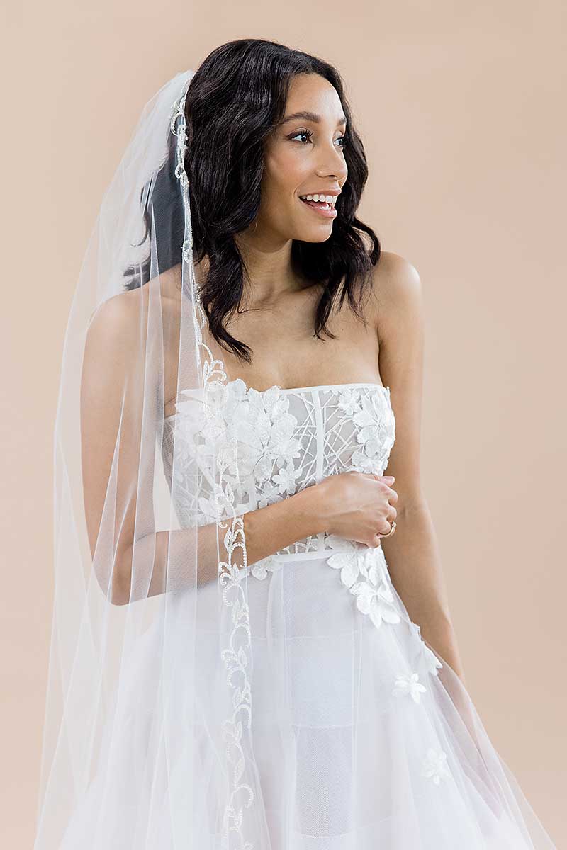 Side front view of bride wearing cathedral veil with pearl vine embroidery. Espere by Laura Jayne