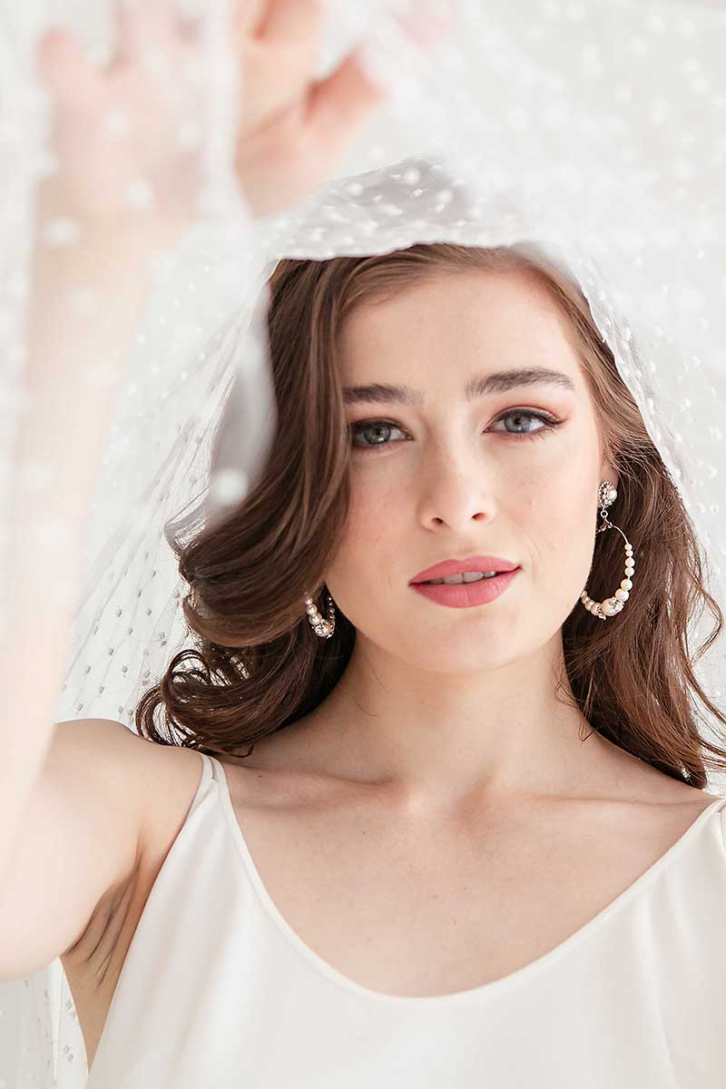 Bride wearing modern pearl hoop earrings while lifting veil