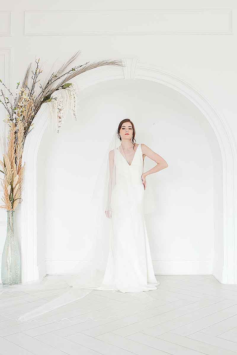 Full view of a bride wearing a minimalist ivory tulle two tiered circle cut veil. Marlow Cathedral Drop Veil. Handmade in Canada by Laura Jayne Accessories.