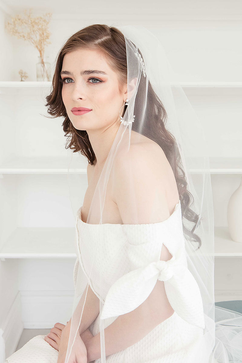 Profile of a seated modern edgy bride wearing Winona Cathedral Veil with Feathers and large hoop bridal earrings. Veil and earrings made in Canada by Laura Jayne Accessories Toronto. 