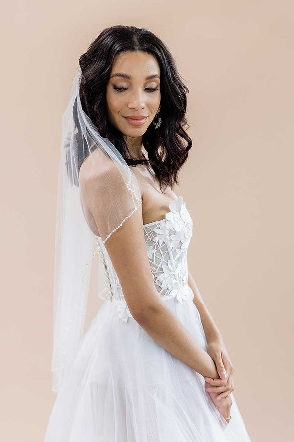 Side front of bride wearing Dea fingertip crystal edge beaded veil by Laura Jayne