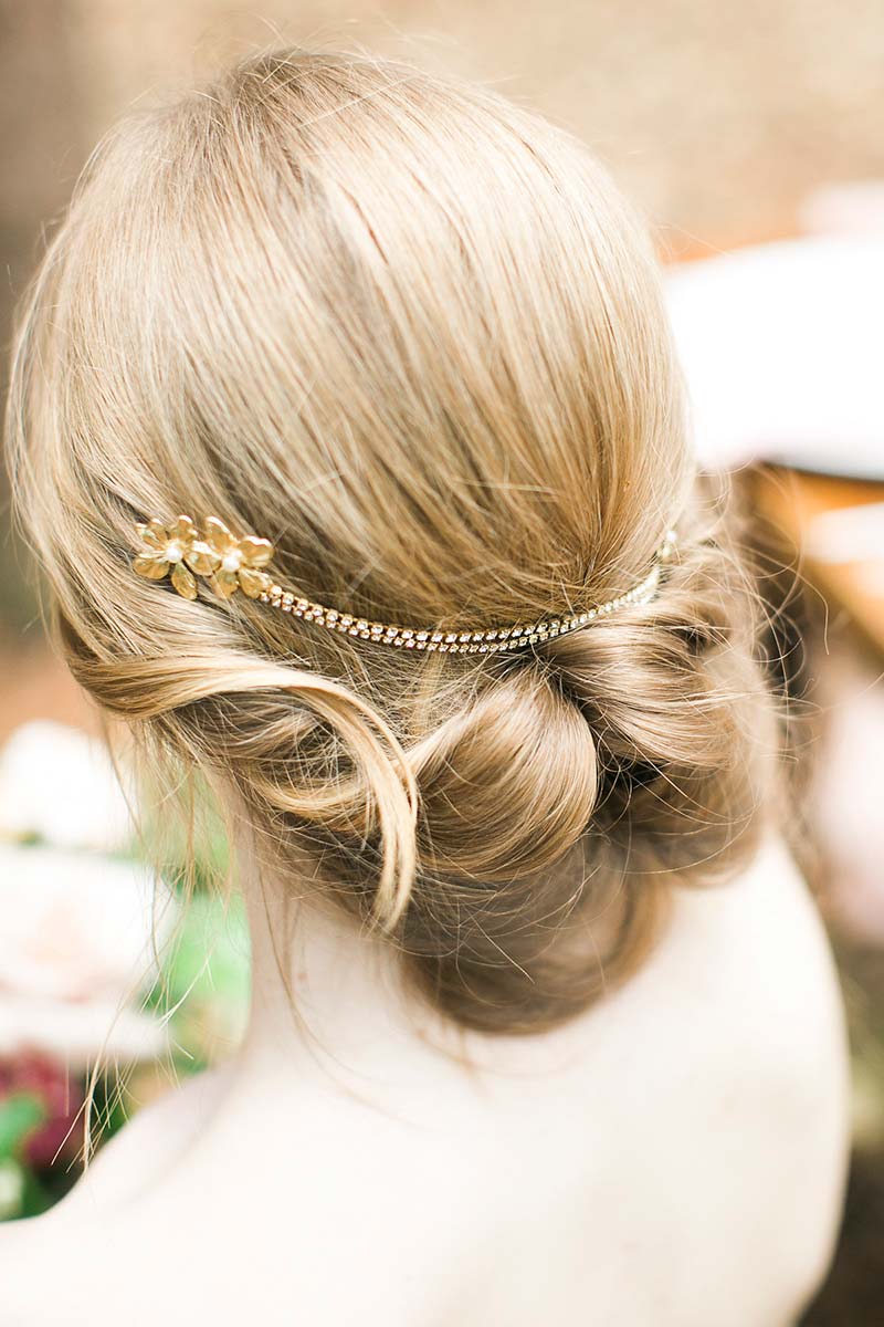 Woman's messy bun hairstyle with chain headpiece with gold blossoms