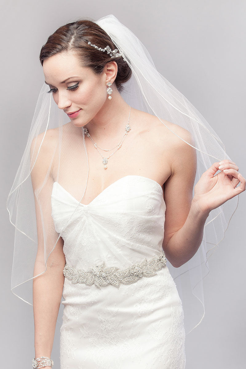 Classic bride looking down wearing a simple minimalist Opulence Two Tier Fingertip cord edge veil by Laura Jayne. Handcrafted in Toronto, Canada.