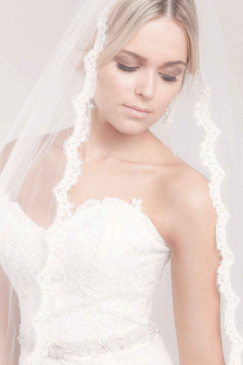 Modern romantic bride looking down wearing a cathedral length veil with French Alencon lace scalloped border. Promise Lace Cathedral Veil by Laura Jayne Accessories Toronto. Handcrafted in Canada.