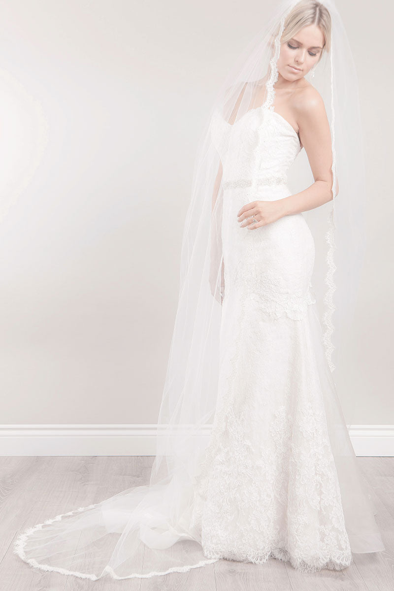 Full length view of a beautiful modern bride wearing a timeless classic long veil with French Alencon lace scalloped border, hand-beaded crystals and romantic floating appliques on the train. Promise Lace Cathedral Veil. Made in Toronto, Canada by Laura Jayne Accessories..