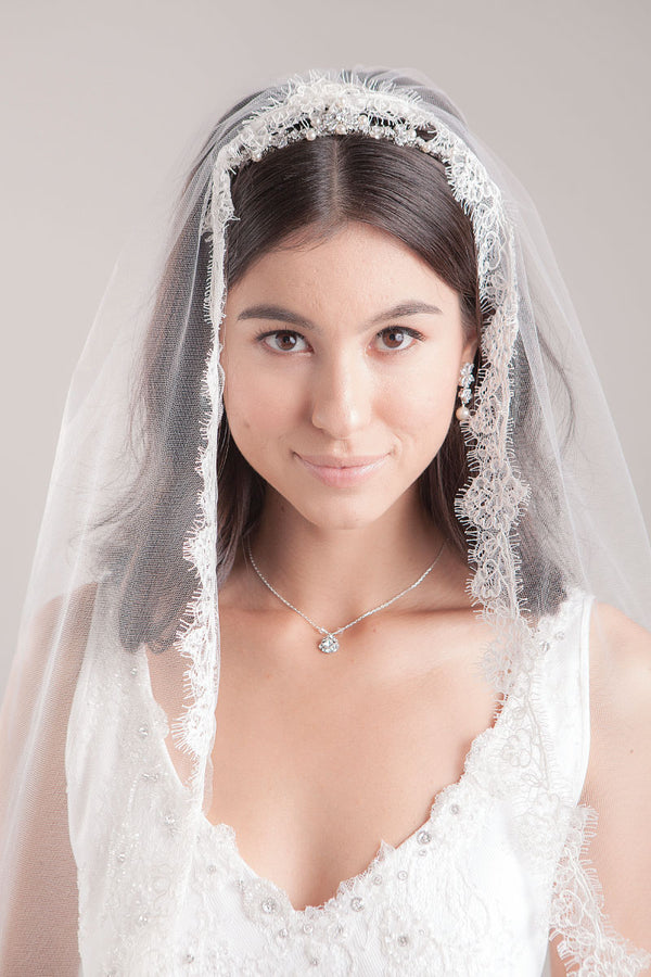 Romantic bride wearing a classic mantilla veil with French Alencon floral lace framing her face. Hayley Fingertip Alencon Mantilla Veil by Laura Jayne. Handcrafted in Canada.