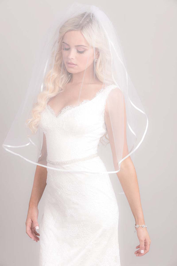 Modern romantic bride wearing a sheer fingertip length blusher veil over her face. Erin Ribbon Edge Fingertip Veil by Laura Jayne. Handcrafted in Toronto, Canada.